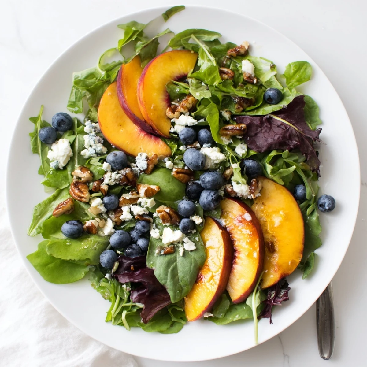Vibrant blueberry peach feta salad topped with toasted pecans and honey balsamic vinaigrette on a bed of fresh salad greens