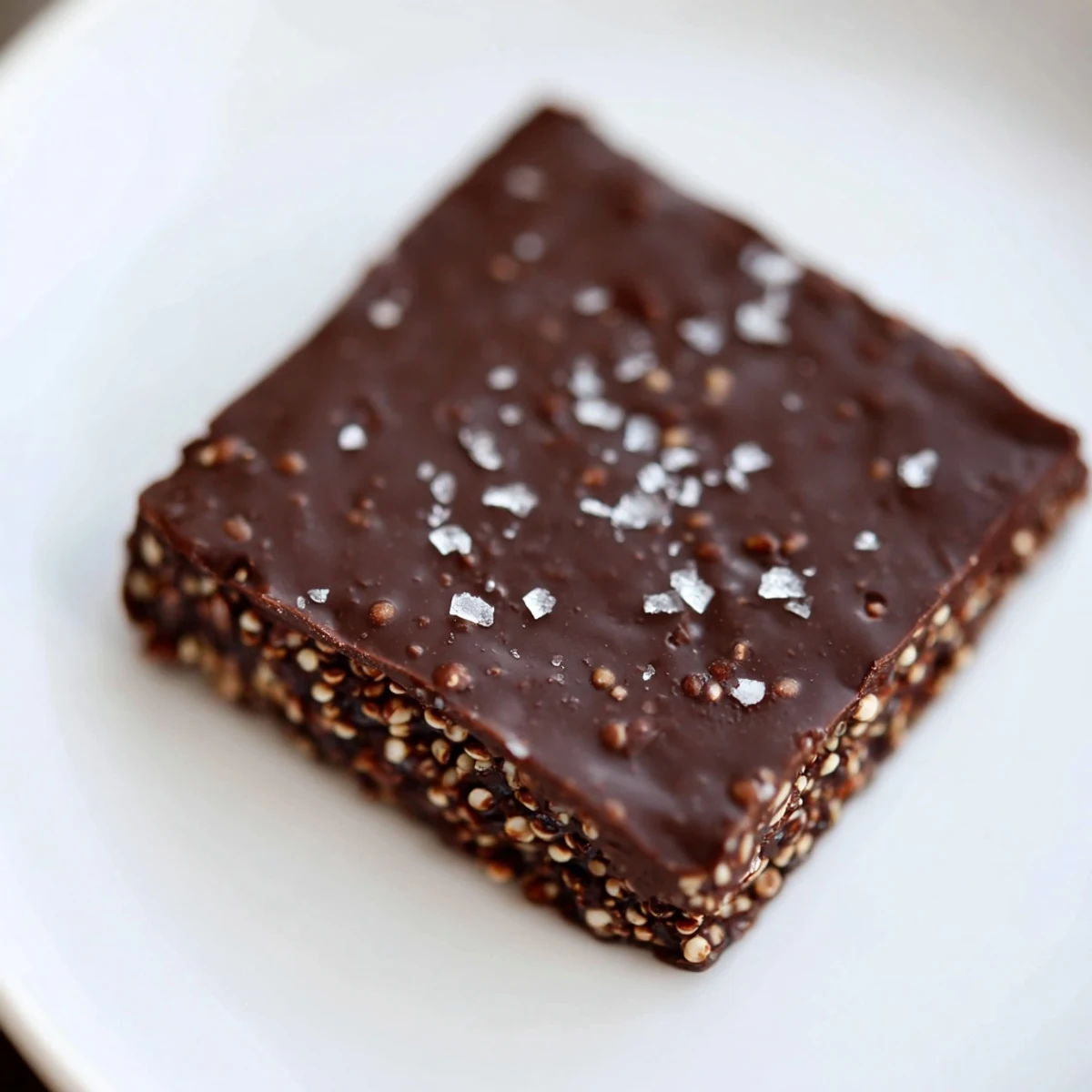Golden dark chocolate quinoa crisps arranged on a white plate, featuring glossy chocolate coating and crunchy toasted quinoa texture
