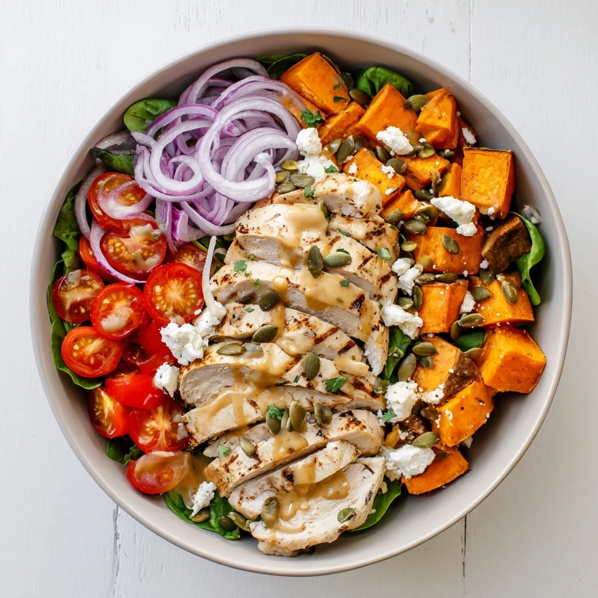 Juicy maple Dijon chicken breast strips resting atop roasted sweet potato cubes and greens in this wholesome bowl