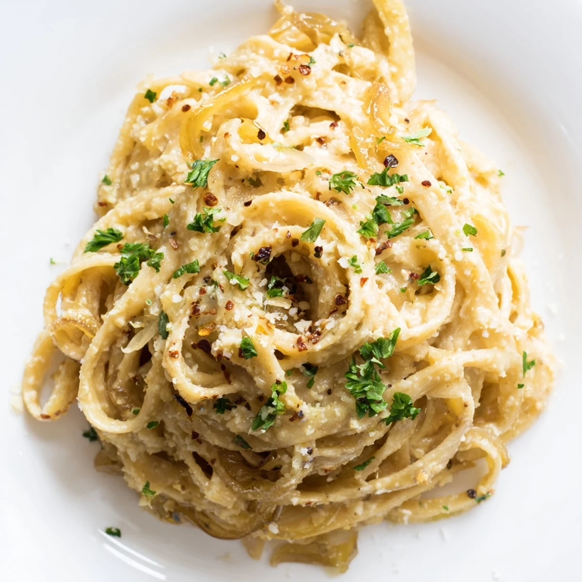 Creamy Sweet Heat Caramelized Onion Fettuccine twirled on a fork with golden brown onions and fresh parsley garnish