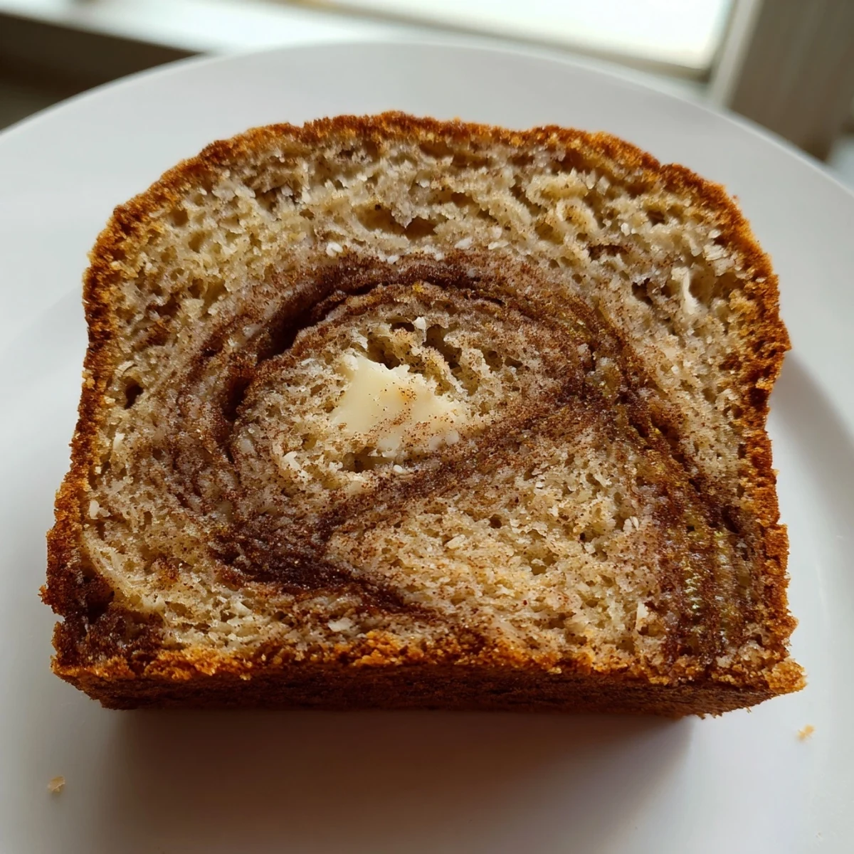 Warm slice of cinnamon sugar swirl banana bread with visible marbled cinnamon layers on rustic wooden board