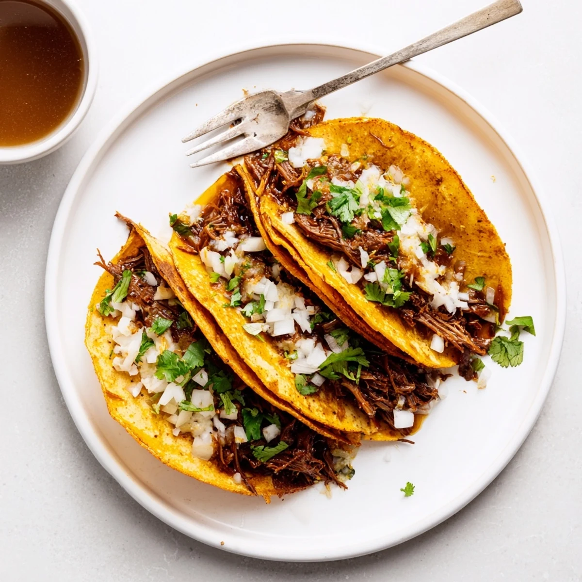Golden birria tacos dipped in rich red consommé with a fresh lime wedge
