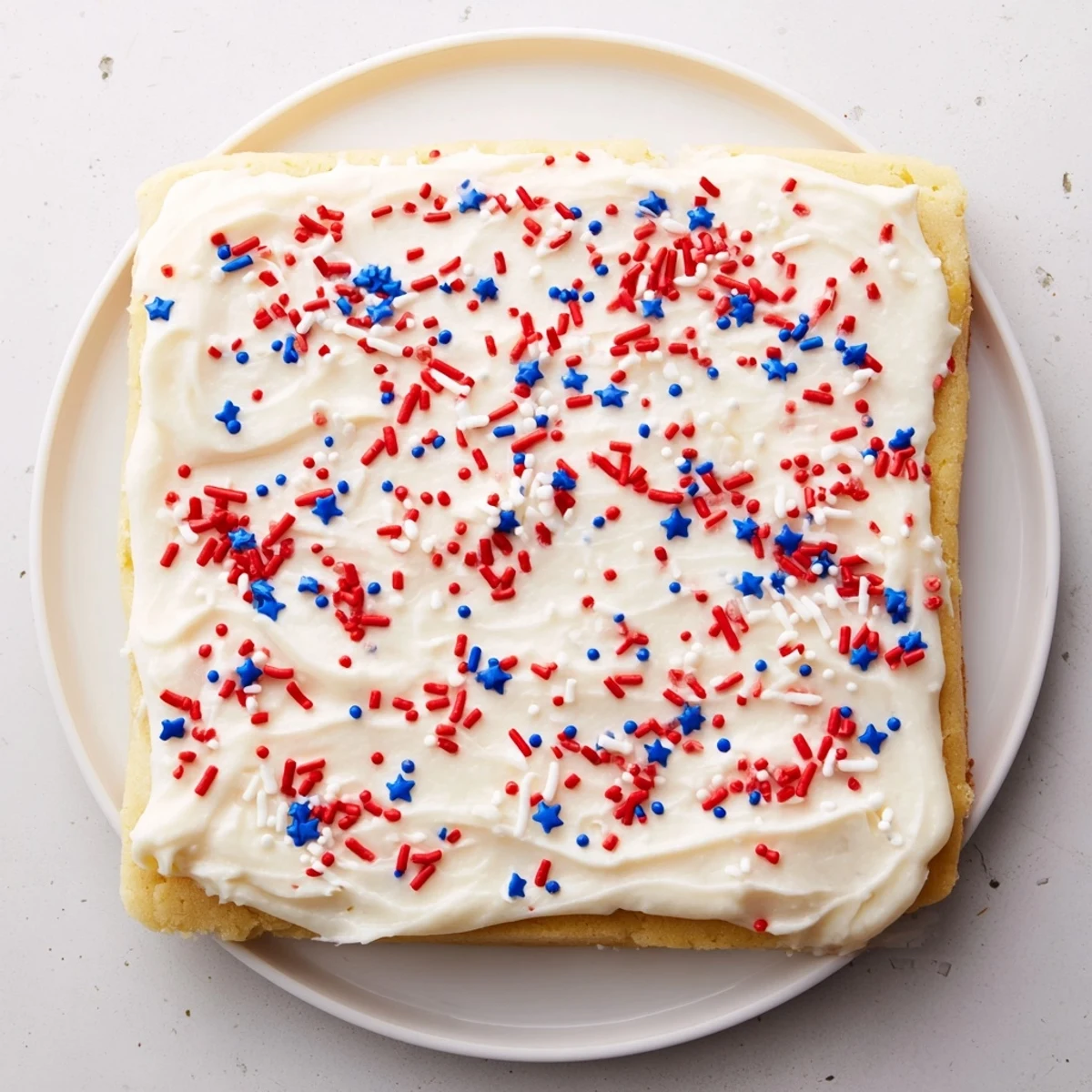 Homemade 4th of July sugar cookie bars with velvety vanilla buttercream frosting and starry red white blue sprinkles ideal for summer parties