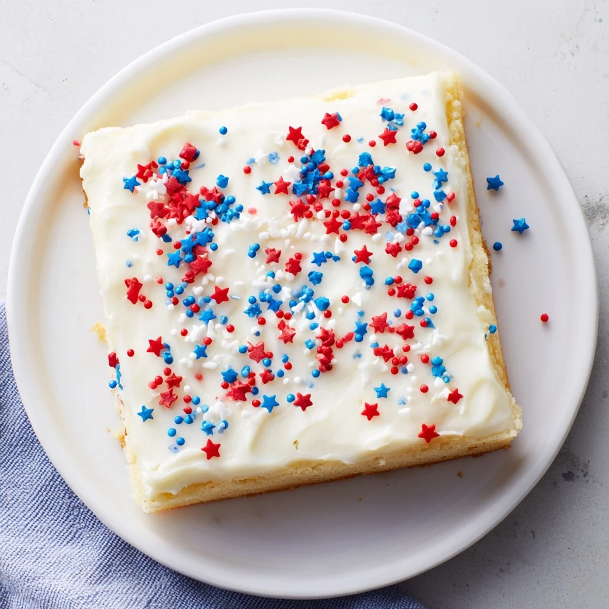 Golden sugar cookie bars spread with fluffy white frosting and decorated with colorful festive sprinkles perfect for your 4th of July dessert table