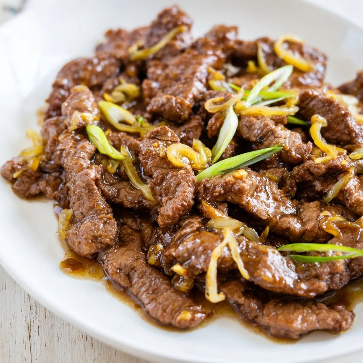 Steaming bowl of crispy beef and onion stir fry garnished with fresh green onions