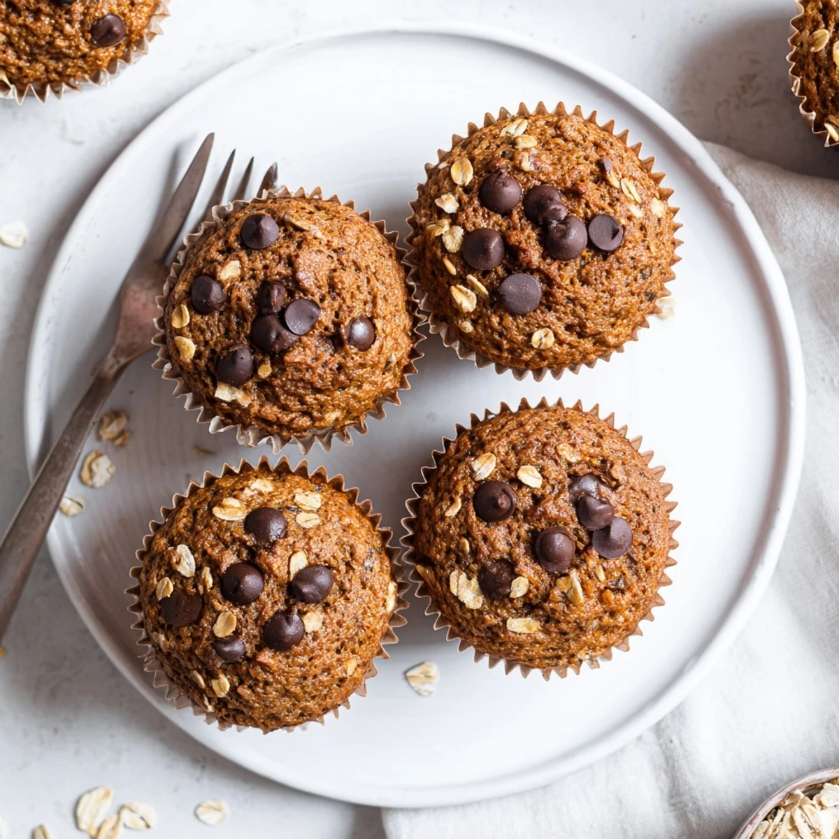 Batch of twelve homemade banana chocolate chip muffins with oats cooling in a paper-lined tin