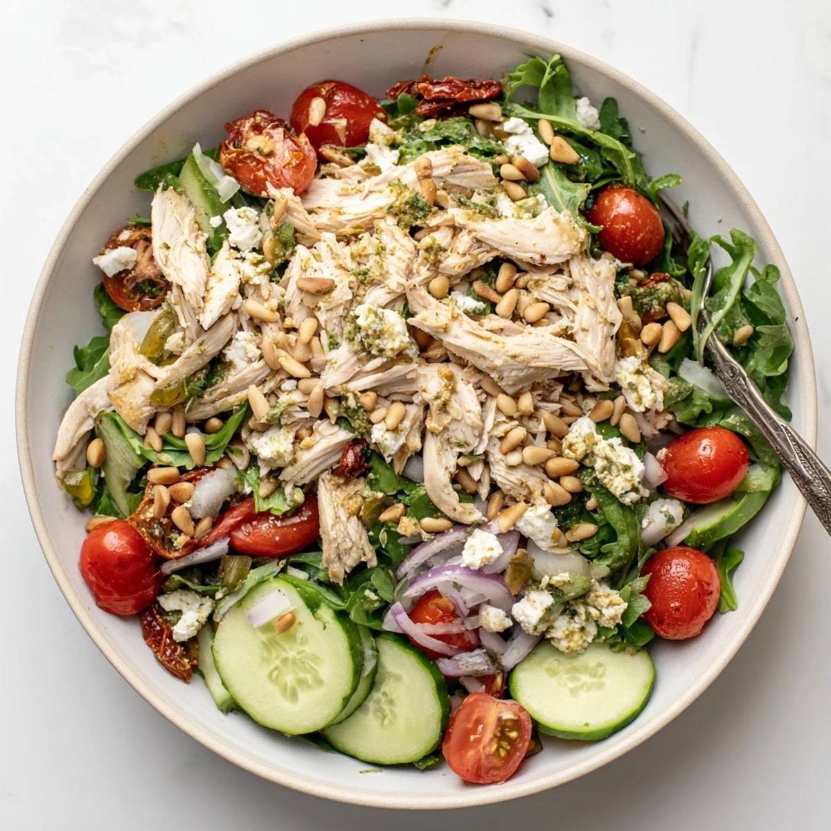 Fresh sun dried tomato chicken salad plated with crisp arugula, red onion, pine nuts, and tangy balsamic dressing