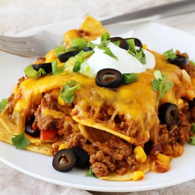Warm Cheesy Nacho Casserole topped with sour cream, cilantro, and sliced jalapeños
