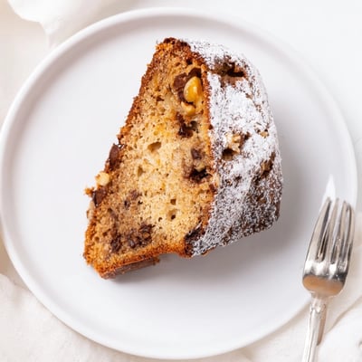 Slice of moist Banana Bread Cake Recipe on plate, walnuts and powdered sugar